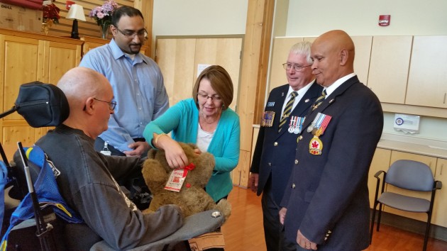 Jason Jaswal, John Scott and Bruce Gabriel look on as MLA Shirley Bond adjusts Spinoza Bear for resident Darryl Wolfe