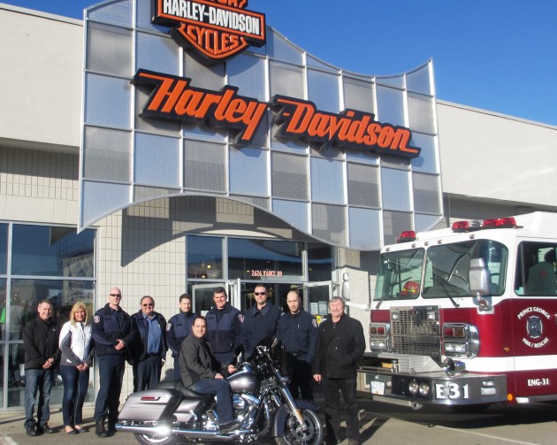 Photo (L-R): Darcy Bryant - Spirit of the North Board Director, Judy Neiser – CEO Spirit of the North, Greg Houston – Spirit of the North Board Director and PG Firefighter, 5 local PG Firefighters and Len Hall - Owner of the Harley Davidson PG Store with winner Kevin Girard sitting on winning motorcycle.