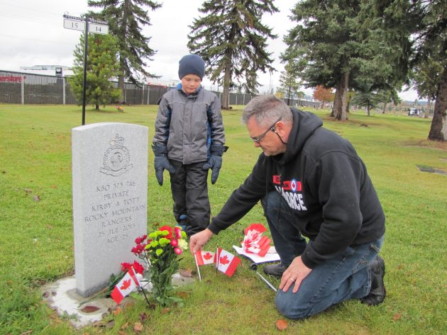 Jayden Brideau watches as Neil Boyes places flag on grave of Private Kirby Tott